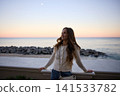 Carefree Woman Stretches Her Arms By The Sea At Dusk 141533782