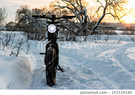 Robust electric fat bike with a bright headlight on a snowy winter path at sunset, perfect for off-road adventures and frosty rides 141534190