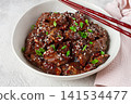 Crispy beef, with green onions and sesame seeds, in a bowl with chopsticks, on a textured surface, on a light background, no people 141534477
