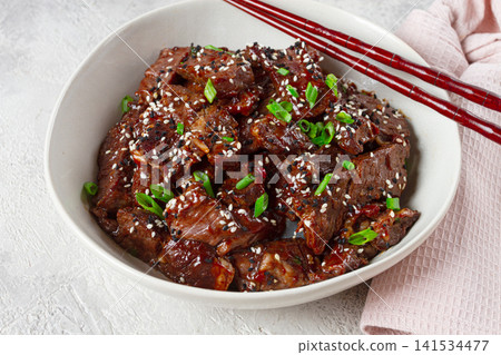 Crispy beef, with green onions and sesame seeds, in a bowl with chopsticks, on a textured surface, on a light background, no people Crispy beef, with green onions and sesame seeds, in a bowl with chopsticks, on a textured surface, on a light background, no people 141534477