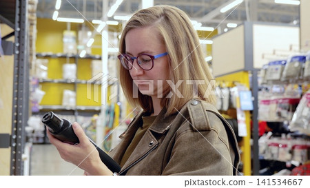 Customer carefully selecting a thermo bottle in a hardware store, reading the label before buying 141534667