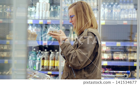 Young woman compares food products and reads labels while grocery shopping in a supermarket Young woman compares food products and reads labels while grocery shopping in a supermarket 141534677