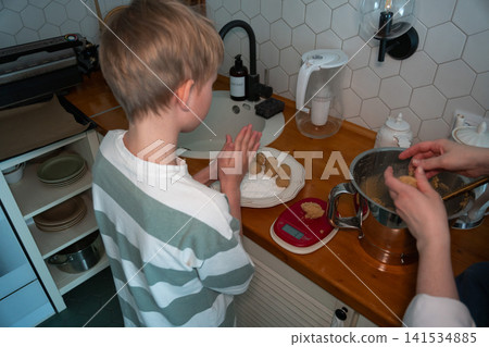 Child shapes cookie dough while adult prepares baking mixture in cozy home kitchen with homemade ingredients and family recipe. Childhood, home cooking, learning, parenting, lifestyle, family 141534885