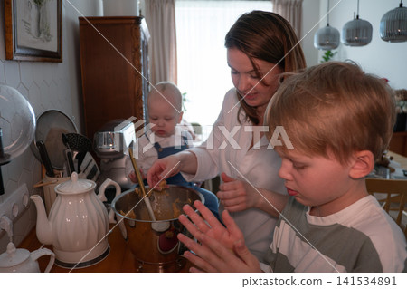 Young mother and two children prepare homemade dough together in cozy kitchen while baking family meal at home. Family, parenting, childhood, cooking, bonding, education, lifestyle, togetherness Young mother and two children prepare homemade dough together in cozy kitchen while baking family meal at home. Family, parenting, childhood, cooking, bonding, education, lifestyle, togetherness 141534891