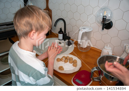 Child shapes cookie dough while adult prepares baking mixture in cozy home kitchen with homemade ingredients and family recipe. Childhood, home cooking, learning, parenting, lifestyle, family Child shapes cookie dough while adult prepares baking mixture in cozy home kitchen with homemade ingredients and family recipe. Childhood, home cooking, learning, parenting, lifestyle, family 141534894