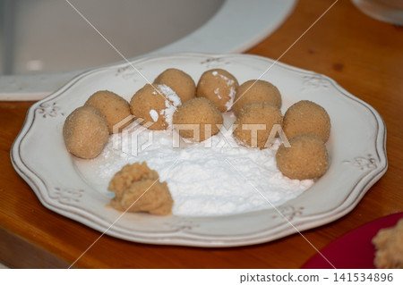 Homemade almond cookie dough balls rest on powdered sugar before baking on decorative plate in family kitchen. Home baking, dessert, recipe, pastry preparation, food styling, cooking, lifestyle Homemade almond cookie dough balls rest on powdered sugar before baking on decorative plate in family kitchen. Home baking, dessert, recipe, pastry preparation, food styling, cooking, lifestyle 141534896