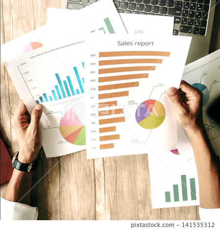 Businessperson reviews financial graphs on a wooden workspace Businessperson reviews financial graphs on a wooden workspace 141535312