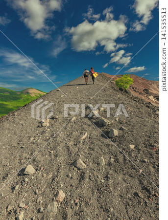 Rear view of two tourists climbing Cerro Negro with a beautiful landscape in the background. Landscape of tourists hiking to the summit of Cerro Negro volcano Rear view of two tourists climbing Cerro Negro with a beautiful landscape in the background. Landscape of tourists hiking to the summit of Cerro Negro volcano 141535513