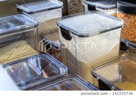 Clear plastic containers filled with flour and grains. Storing dry goods in airtight containers in a well-organized kitchen cabinet drawer Clear plastic containers filled with flour and grains. Storing dry goods in airtight containers in a well-organized kitchen cabinet drawer 141535736