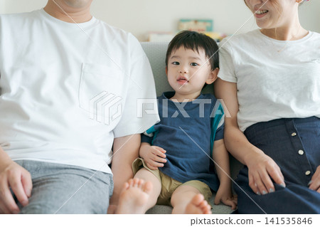 A boy sitting on a sofa with his parents. A boy sitting on a sofa with his parents. 141535846