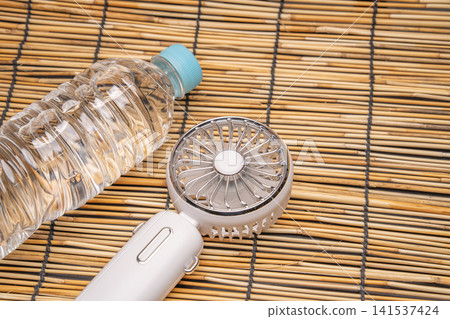 一台白色便攜式風扇和一瓶飲用水,描繪了一幅夏日應對酷暑的場景。 一台白色便攜式風扇和一瓶飲用水,描繪了一幅夏日應對酷暑的場景。 141537424