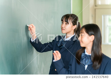 A female junior high school student writing with chalk on a blackboard in the classroom A female junior high school student writing with chalk on a blackboard in the classroom 141537640