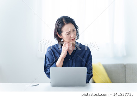 一位表情憂慮的中年婦女正在辦公桌前工作。 141537733