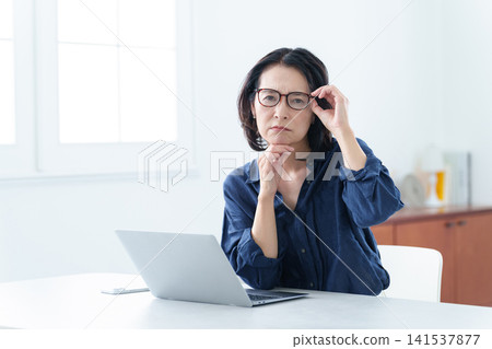 戴著老花眼鏡的中年婦女正在使用電腦。 戴著老花眼鏡的中年婦女正在使用電腦。 141537877