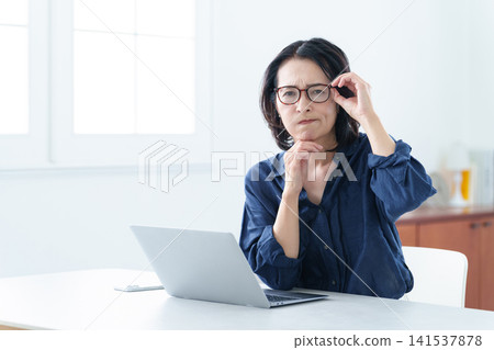 戴著老花眼鏡的中年婦女正在使用電腦。 141537878
