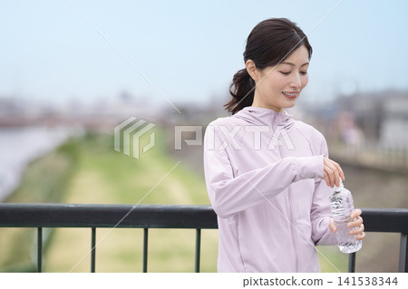 A middle-aged woman drinking bottled water while walking. 141538344
