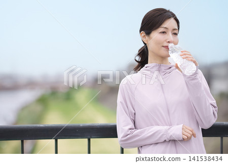 一位中年婦女邊走邊喝瓶裝水。 一位中年婦女邊走邊喝瓶裝水。 141538434