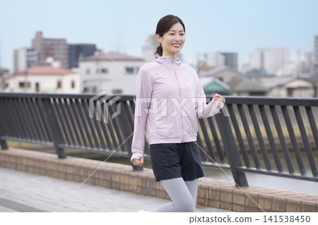 一位中年婦女身穿運動服沿著河岸行走。 一位中年婦女身穿運動服沿著河岸行走。 141538450