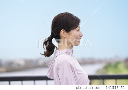 一位中年婦女身穿運動服沿著河岸行走。 一位中年婦女身穿運動服沿著河岸行走。 141538451