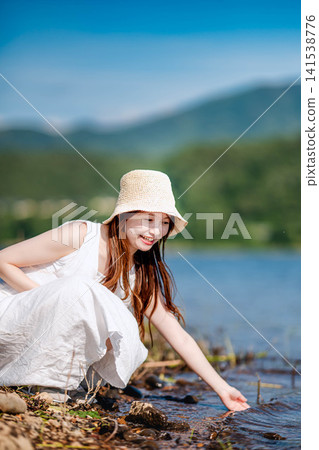 一位身穿白色洋裝的女子向湖邊伸出手。 一位身穿白色洋裝的女子向湖邊伸出手。 141538776