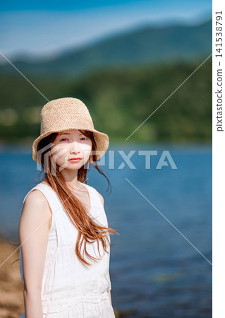 A woman in a white dress smiles against the backdrop of a summer lake. A woman in a white dress smiles against the backdrop of a summer lake. 141538791