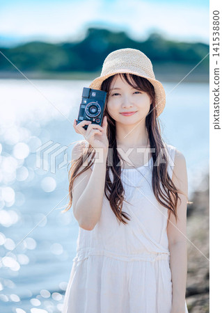 一位身穿白色連身裙的女子手持底片相機,背景是湖泊。 一位身穿白色連身裙的女子手持底片相機,背景是湖泊。 141538800