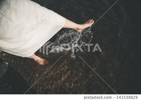 The feet of a woman kicking water barefoot by the lake. 141538829