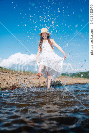 一名身穿白裙的女子走過淺水，濺起陣陣水花。 141538846