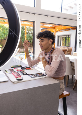 Male makeup artist holding mascara wand applying makeup palettes under ring light Male makeup artist holding mascara wand applying makeup palettes under ring light 141539002