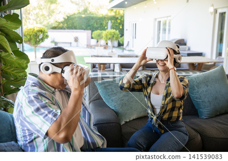 Senior couple experiencing virtual reality wearing headsets on outdoor sofa at backyard patio Senior couple experiencing virtual reality wearing headsets on outdoor sofa at backyard patio 141539083