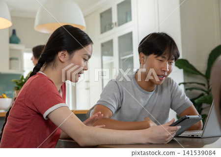 Diverse family collaborating over tablet and laptop in kitchen beside bowl of fruit 141539084