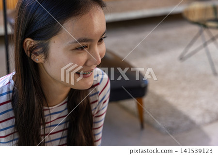 Asian woman sitting on carpet in living room with leather bench and accent chair Asian woman sitting on carpet in living room with leather bench and accent chair 141539123