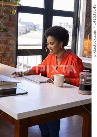 African american woman working at office desk with keyboard, french press African american woman working at office desk with keyboard, french press 141539149