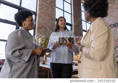 Diverse coworkers discussing ideas at office holding tablet and smartphone near laptop, plants Diverse coworkers discussing ideas at office holding tablet and smartphone near laptop, plants 141539150