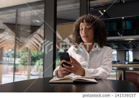 Woman sitting at black table in modern cafe with smartphone and studying notebook, copy space Woman sitting at black table in modern cafe with smartphone and studying notebook, copy space 141539157