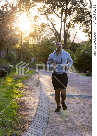 Man jogging along curving paved path with brick edging in park under dappled sunlight Man jogging along curving paved path with brick edging in park under dappled sunlight 141539181