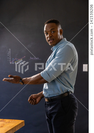 African american man in business attire gesturing toward line graph on board in classroom 141539206