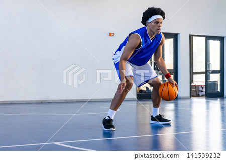 African american teen athlete dribbling orange basketball on gym wearing basketball jersey 141539232