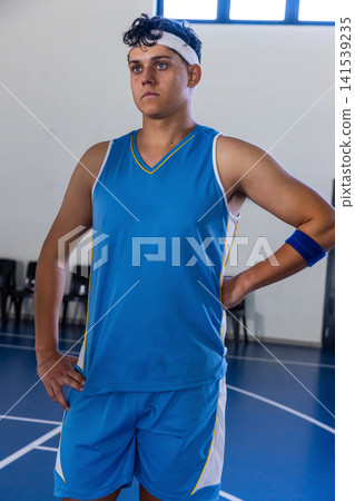 Teenage male basketball player standing with hands on hips on school court wearing blue jersey Teenage male basketball player standing with hands on hips on school court wearing blue jersey 141539235