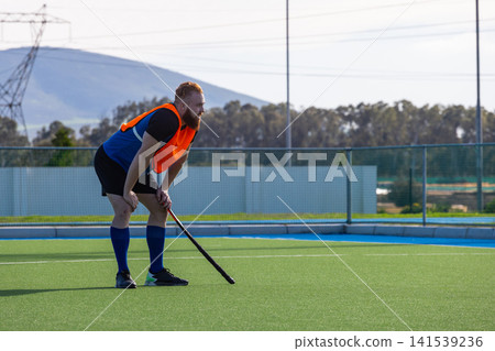 Male athlete in orange bib and holding field hockey stick on artificial turf field, copy space Male athlete in orange bib and holding field hockey stick on artificial turf field, copy space 141539236