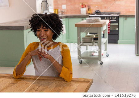 African american woman sitting and smiling at dining table next to mobile kitchen island African american woman sitting and smiling at dining table next to mobile kitchen island 141539276