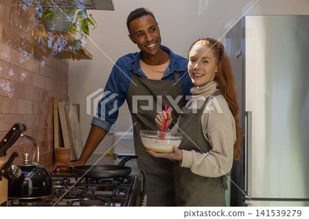 Diverse couple cooking in home kitchen, mixing batter in glass bowl with spatula Diverse couple cooking in home kitchen, mixing batter in glass bowl with spatula 141539279