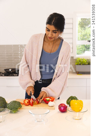 Indian woman chopping red bell pepper with chef's knife on cutting board at home kitchen island Indian woman chopping red bell pepper with chef's knife on cutting board at home kitchen island 141539308