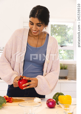 Asian woman slicing red bell pepper on cutting board with broccoli and onion in modern kitchen Asian woman slicing red bell pepper on cutting board with broccoli and onion in modern kitchen 141539310