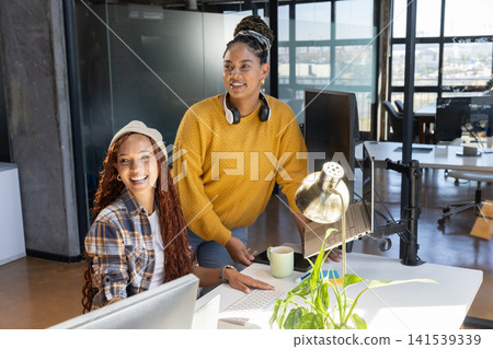 Diverse female colleagues collaborating at modern office desk using desktop monitor and laptop 141539339