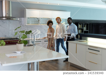Diverse group touring kitchen with agent in business attire with tablet at island with paperwork Diverse group touring kitchen with agent in business attire with tablet at island with paperwork 141539340
