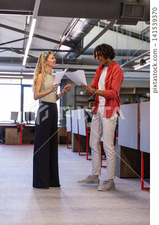 Diverse coworkers reviewing printed documents near desks and monitors in open-plan office Diverse coworkers reviewing printed documents near desks and monitors in open-plan office 141539370
