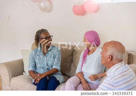 Diverse senior friends chatting on beige couch in living room at home with balloons, pillow Diverse senior friends chatting on beige couch in living room at home with balloons, pillow 141539371