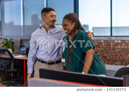 Diverse coworkers in business attire linking arms, leaning toward screen at office desks Diverse coworkers in business attire linking arms, leaning toward screen at office desks 141539373