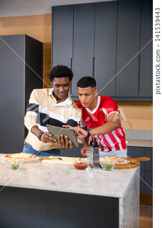 Diverse male friends preparing pizzas at marble kitchen island using tablet and wooden pizza boards Diverse male friends preparing pizzas at marble kitchen island using tablet and wooden pizza boards 141539443